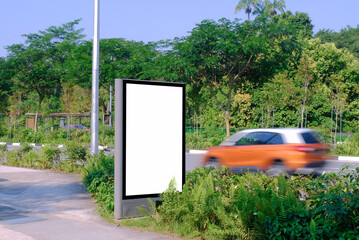 Advertising billboard by the road, with passing speeding car in motion blur. Blank vertical mock up...