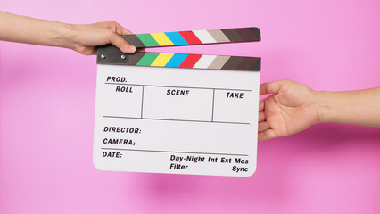 Hand is holding clapper board and sending clapperboard to other hand on pink background.
