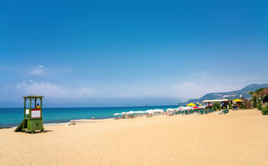 Wide sandy beach with golden sand and a lifeguard booth against a bright blue sky in Mediterranean resort Turkey.