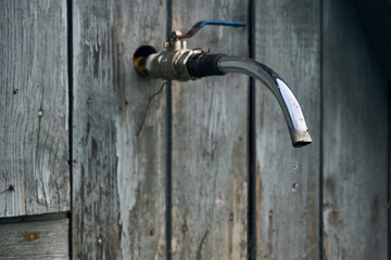 A wooden wall from which sticks out a faucet from which water drips. Gutter for washing or watering, garden appliances