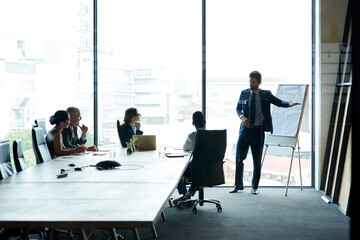 Executive having a presentation in a boardroom at a modern office. Businesspeople listening to a serious business leader presenting a vision, thinking and mission for a project at the workplace. - Powered by Adobe