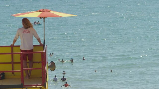 Lone Lifeguard Looks Out To Sea As People Play In The Waters, In Slow Motion - Space For Text