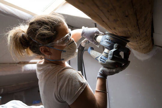 Woman carpenter using electric sander for wood