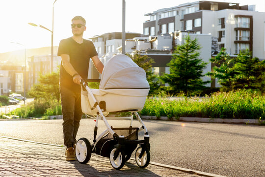 a young father walks with a stroller down the street. Walk with the child in the fresh air.