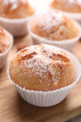 Tasty muffins powdered with sugar on wooden board, closeup