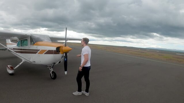 Pilot Standing In Front Of A Parked Cessna 172 Skyhawk Plane On A Cloudy Day. wide, slow motion