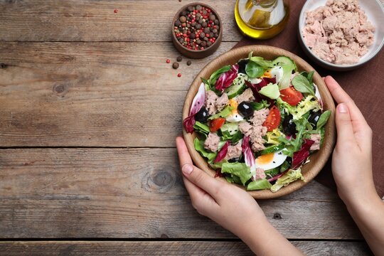 Woman holding bowl of delicious salad with canned tuna at wooden table, top view. Space for text