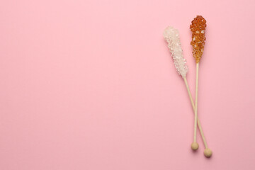 Wooden sticks with sugar crystals and space for text on pink background, flat lay. Tasty rock candies
