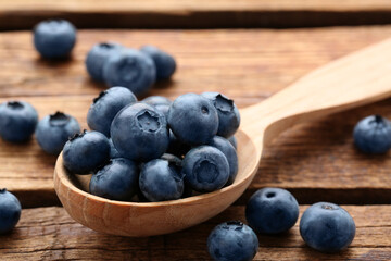 Spoon with tasty fresh blueberries on wooden table, closeup