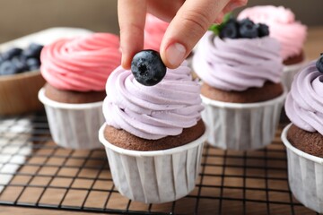 Woman decorating cupcake with fresh blueberry at table, closeup