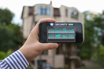 Man using home security application on smartphone in front of house outdoors, closeup