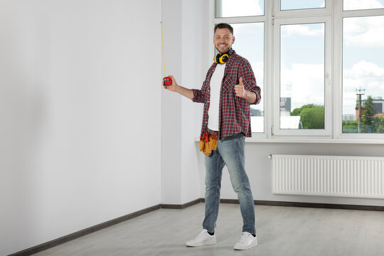 Handsome worker with measuring tape in empty room, space for text