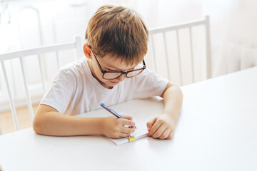 A boy in eyeglasses writes with a pen in a notebook.