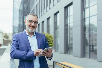 Portrait of successful businessman outside office building with tablet in hands, investor in...
