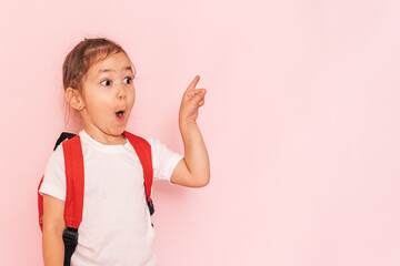 Surprised little girl with a red briefcase points her finger against a pink background.