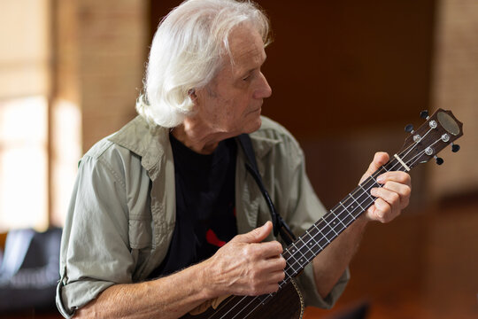 grey haired man strumming a ukulele