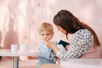 Mom and little cute daughter in the cafe. Mom wipes daughter's face. Mother with a napkin removes ice cream from the face of a child