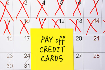 The phrase Pay off Credit cards written in black text on a yellow sticky note posted to a calendar...