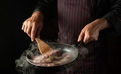The chef is frying sausages for hot dogs in a frying pan. Close-up of a cook hands with a hot pan in the kitchen. Free space for advertising.