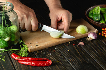 Fototapeta Slicing onions on a cutting board by the hands of a cook for pickling or salt in a jar with cucumbers and spices. Menu for restaurant or hotel obraz