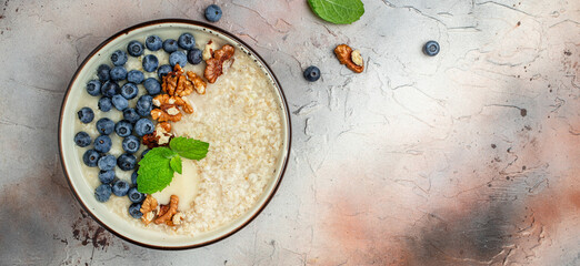 Oatmeal porridge in a bowl with fresh blueberries and nuts on a light table. Healthy breakfast. Super food healthy eating vegetarian vegan food. Long banner format. top view - obrazy, fototapety, plakaty