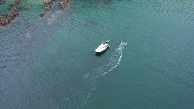 Wide aerial view orbiting a jet ski and small boat off the Cornish coast of the UK
