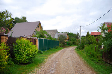 A simple rural dirt road in Russia. The road in the country village. Rustic landscape. The road in the village. Country village. Wooden houses. Rural landscape. Summer in the country.