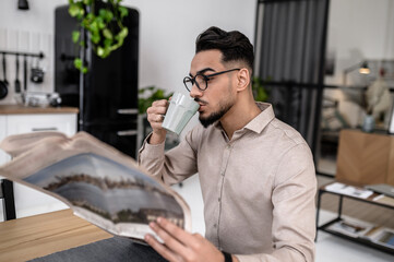 Man drinking coffee reading newspaper sideways to camera