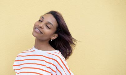 Fototapeta Photo of amazing dark-skinned lady looking towards empty space with a sly smile in a striped t-shirt on a yellow background obraz