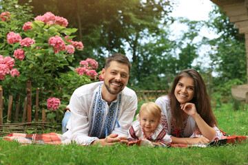 Fototapeta premium Happy family in Ukrainian national clothes on green grass outdoors