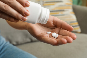 Woman pouring pills from bottle indoors, closeup. Menopause concept