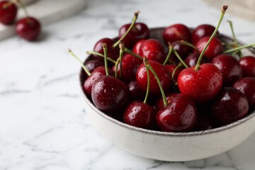 Fresh ripe cherries with water drops in bowl on white marble table, closeup
