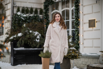 A young girl with long dark hair is shopping for Christmas, holding a craft bag with Christmas tree branches in her hands, walking around the city decorated for Christmas or New Year