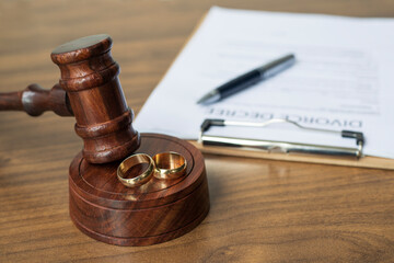 Divorce decree, gavel and rings on warm wooden surface