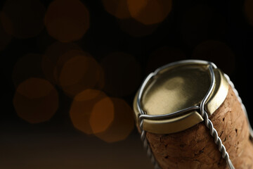 Closeup view of sparkling wine cork and muselet cap against blurred festive lights, space for text....