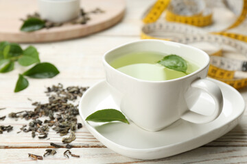 Fototapeta na wymiar Cup of diet herbal tea and measuring tape on white wooden table