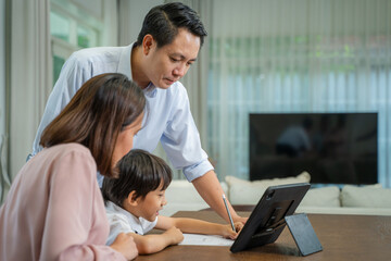 Young boy doing his school homework with Parents,Boy is writing in his book.