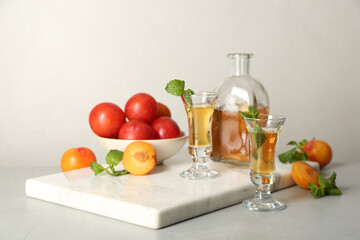 Delicious plum liquor with mint and ripe fruits on light table. Homemade strong alcoholic beverage