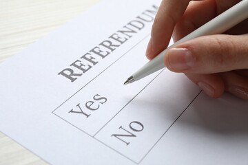 Woman with referendum ballot making decision at white table, closeup - obrazy, fototapety, plakaty