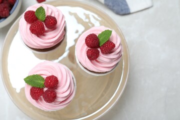 Delicious cupcakes with cream and raspberries on light grey marble table, flat lay