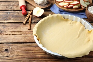 Raw dough and ingredients on wooden table, space for text. Baking apple pie