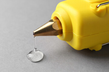 Fototapeta Melted glue dripping out of hot gun nozzle on grey background, closeup obraz