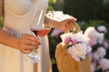Fototapeta Woman with glass of rose wine and straw bag in peony garden, closeup obraz