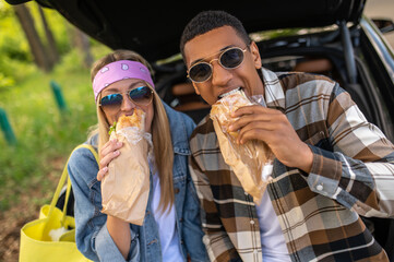 Fototapeta Young man and woman eating sandwiches and looking contented obraz