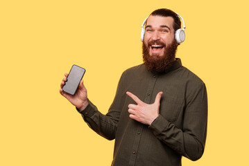 A picture of a man with headphones pointing to his new phone