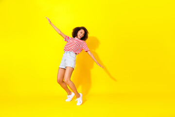 Full size photo of young smiling dancing lady hands wings looking empty space celebrating isolated on yellow color background