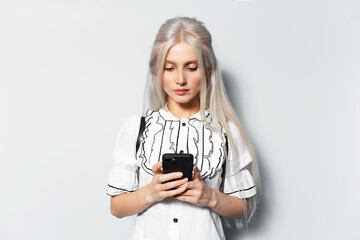 Studio portrait of young blonde pretty girl using smartphone, texting a message, on white background.