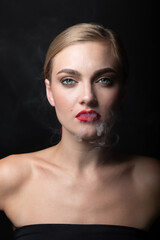 Fashion, style and make-up concept. Close-up studio portrait of beautiful blonde woman blowing smoke from mouth. Model looking to camera with green eyes and seductive look. Red vivid lipstick on lips