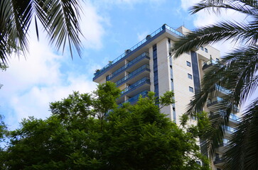 Fototapeta na wymiar Beautiful residential building surrounded by a garden. Modern housing. Israel - high-rise building, flowering and palm trees. Concept: nice place to live, real estate purchase