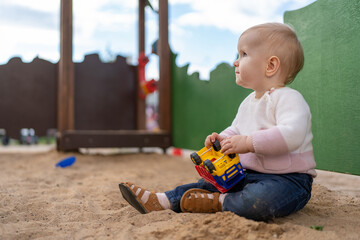Toddler with toy car in sandbox on playground